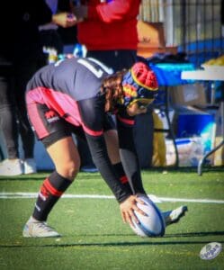 Jugadora de rugby base apoyando el balón para anotar un ensayo en el campo