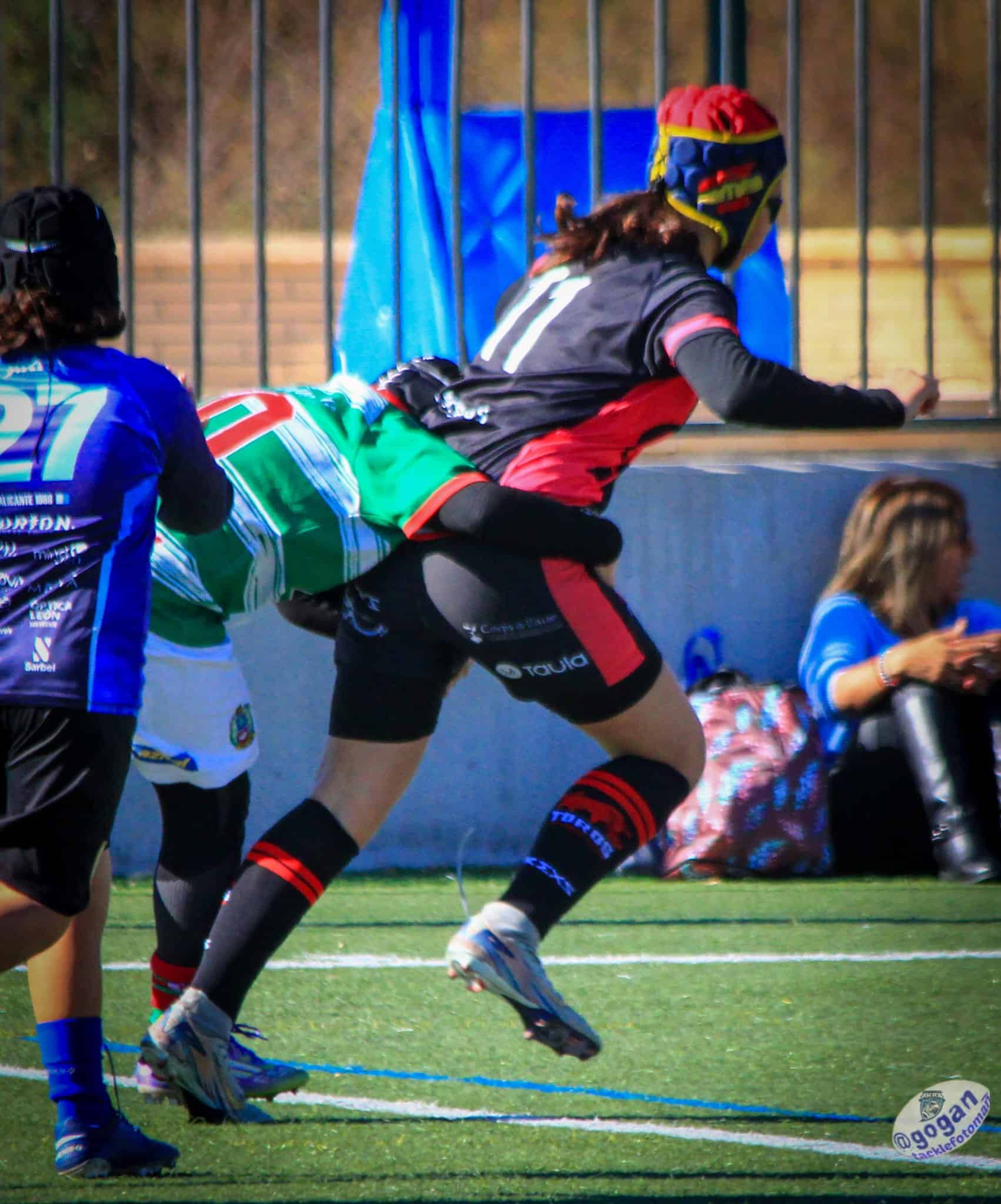 Jugadora de rugby femenino avanzando hacia ensayo mientras recibe un placaje cerca de la línea